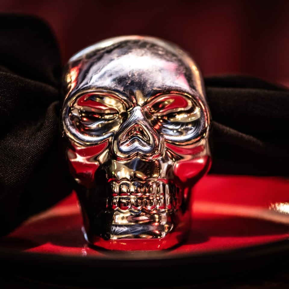 A shiny silver skull sits on a red plate, with a black napkin draped behind it.